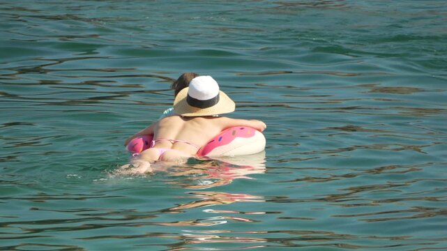 Woman swimming water, girl in pink bikini and straw hat floating on donut inflatable with child.