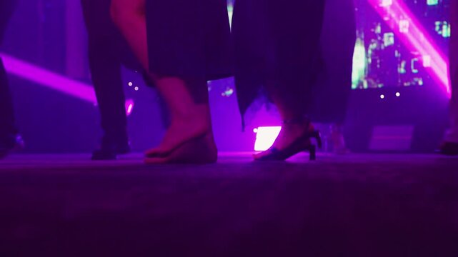 Elegant dancers shift poses under vibrant purple lighting creating festive atmosphere. Luminous stage shines as stylish performers showcase diverse dance moves during energetic night celebration