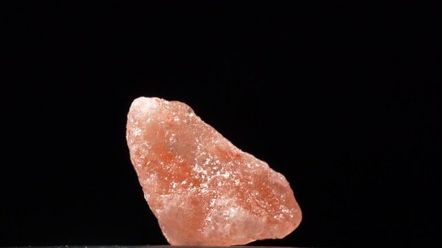 Macro single pink Himalayan rock salt crystal isolated on a black background. Pure natural mineral texture for premium food and spa wellness projects.