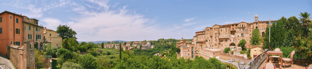Fototapeta premium Panoramic view of Siena Italy with historic old town buildings and green hills under blue sky, scenic European landscape, travel destination with medieval architecture and nature