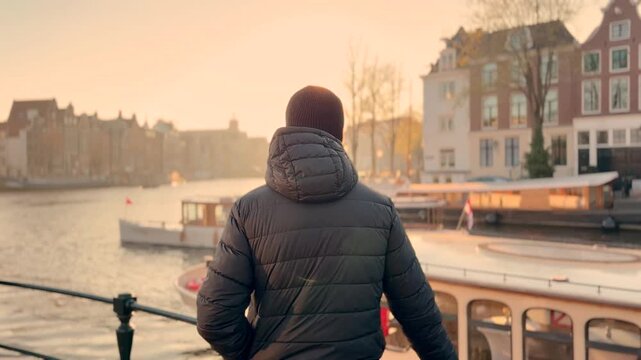 Man in coat watching river and boats at sunset in Amsterdam