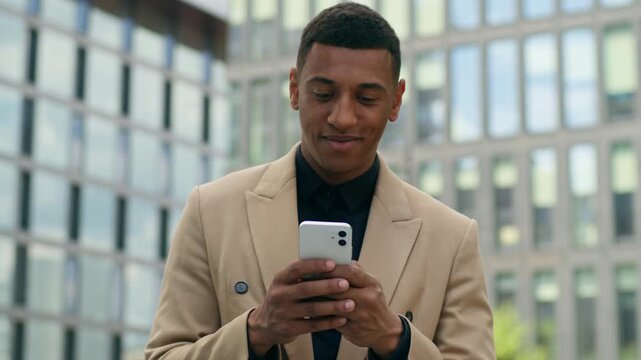 Confident smiling African American business man use smartphone chatting in city downtown outside male entrepreneur investor browsing mobile phone texting social media businessman online communication