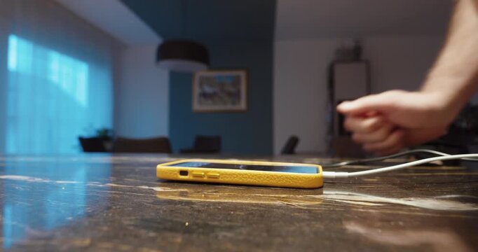 Close-up of a hand plugging a smartphone into a charger on a table at home. Everyday technology use and modern lifestyle.