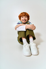 Stylish little boy sits happily on the floor with a joyful smile in trendy fashion attire © Bliss
