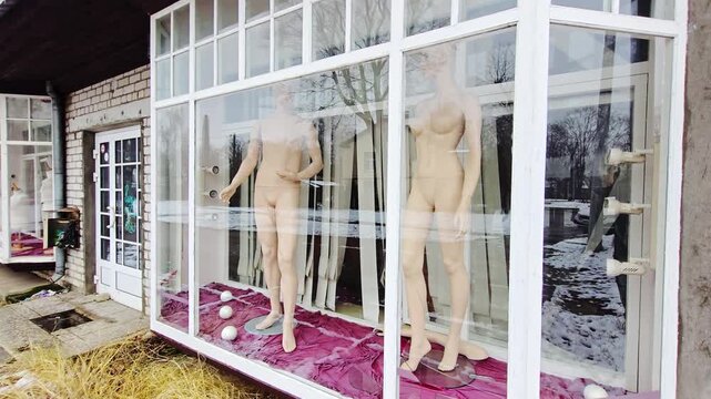 Still mannequins stand behind glass window in silent abandoned shop exterior