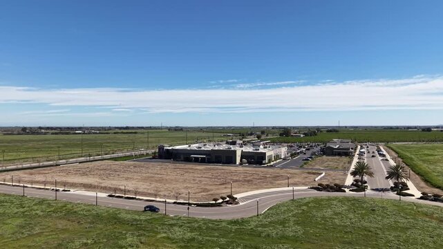 Expansive aerial footage showcasing a modern industrial complex adjacent to verdant agricultural fields and undeveloped land under a clear blue sky in rural California