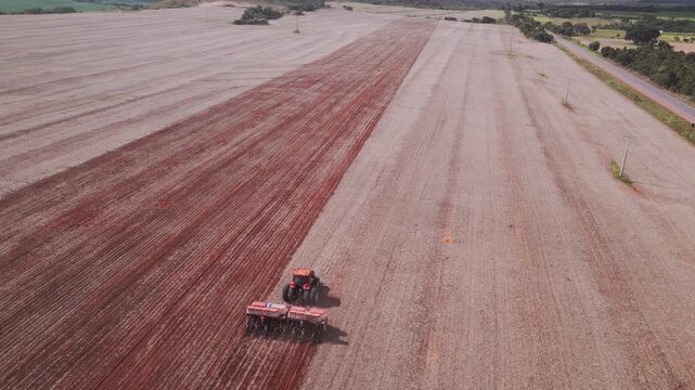 Tractor pulling disc harrow performing soil tillage in Formosa, Goi&aacute;s, Central-West Brazil, preparing seedbed with mechanized cultivation in large-scale agribusiness, drone tracking shot, high angle,
