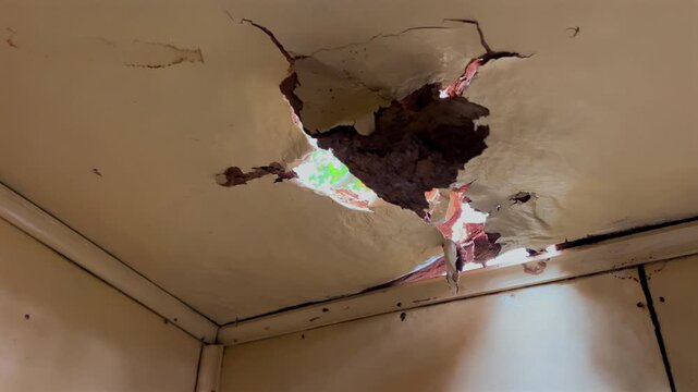 Moisture damaged ceiling reveals holes, cracks and daylight leaking into an indoor corner.