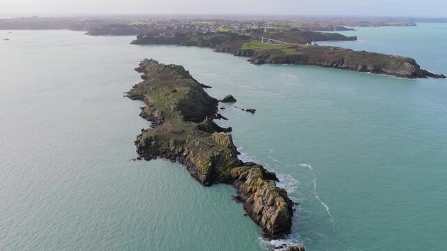 Aerial view of the rocky Pointe du Grouin headland stretching into the turquoise sea under a soft hazy sky in Cancale, Bretagne, France.