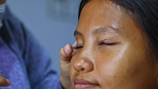 Professional makeup artist applying false eyelashes to asian model