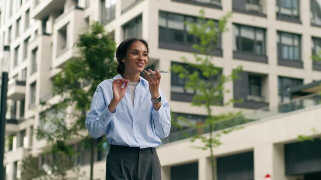 Smiling African American business woman talking smartphone outdoors in city female student businesswoman CEO sending audio message voice mail using loudspeaker walking urban communication technology