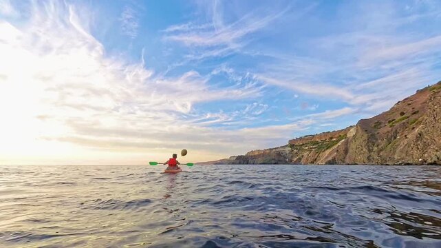 Kayaking sunset ocean adventurer paddles a small boat along rocky sea cliffs during a beautiful golden hour for travel and recreation