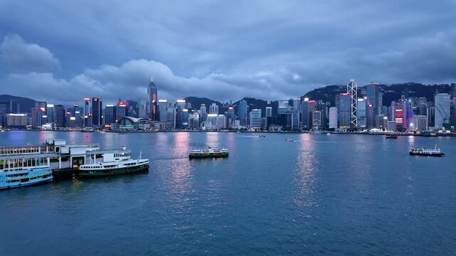 Hong Kong, China: Cinematic panoramic footage of a ferry that crosses the Victoria harbor  between Kowloon Tsim Sha Tsui and Hong Kong island Central at night with a dramatic cloudy sky 