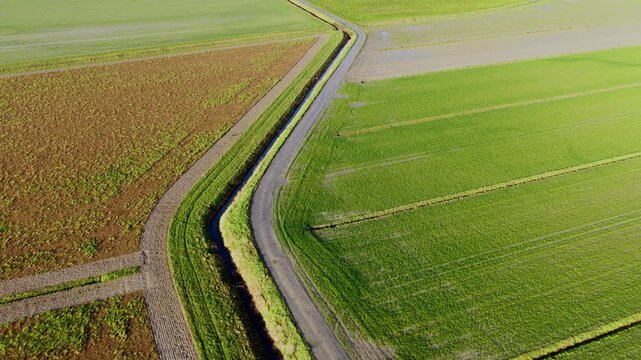 Aerial view of green agricultural fields and a narrow rural road with a drainage ditch in Mont Saint-Michel, Normandy, France.