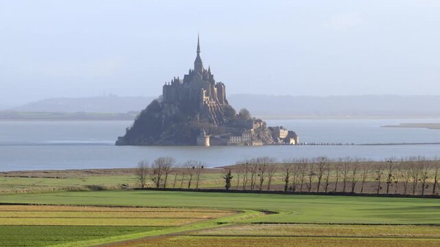 Aerial view of the historic Mont Saint-Michel abbey rising above the tidal bay and green fields in Mont Saint-Michel, Normandy, France.