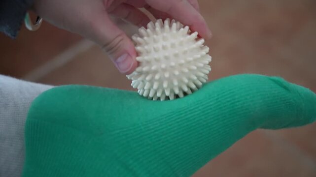 Woman with plantar fasciitis uses a spiky to massage her aching food and heel