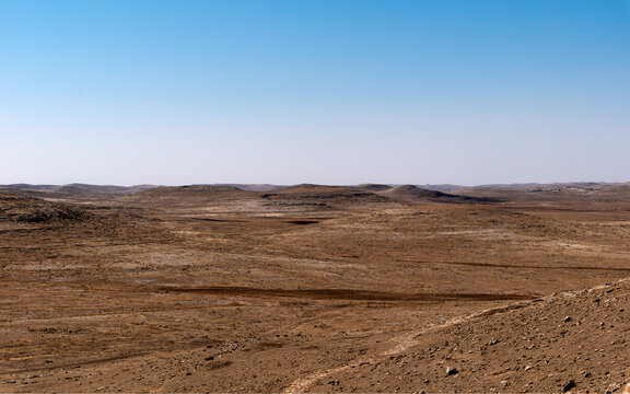 A vast, desolate landscape with dry soil and no vegetation, blue sky, brown earth.