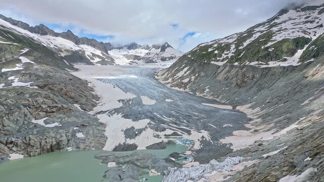 Aerial view of the majestic Rhone Glacier cascading down the rugged, snow-dusted mountains into an icy lake, Obergoms, Valais, Switzerland.