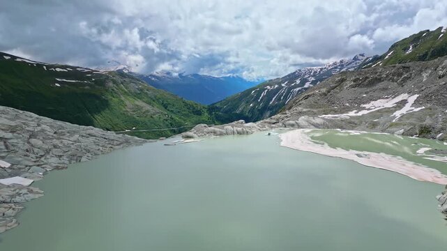 Aerial view of the contrasting textures of the rugged Furka Pass, with a glacial lake against verdant green mountains, Obergoms, Valais, Switzerland.