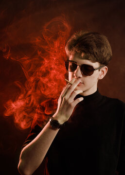 Young man in black turtleneck smoking cigarette in moody red light.
