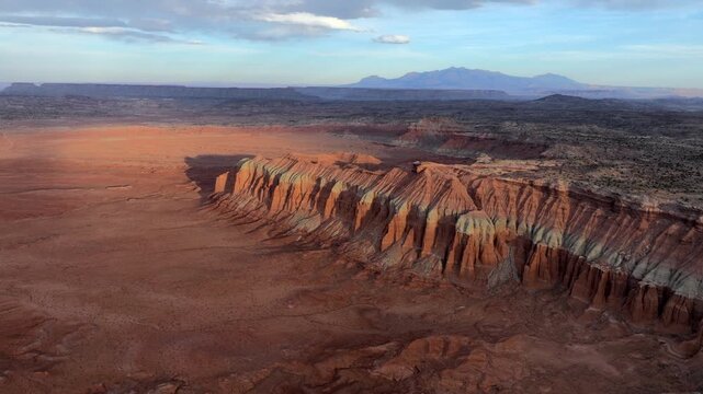 Aerial view of Factory Butte featuring striated rock formations and vast desert plains under a soft sky in Wayne County, Utah, United States.