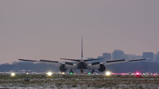 A large passenger airplane seen from behind is landing on a frosty and snowy airport runway at dawn