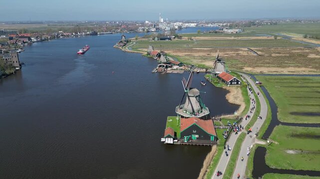 Aerial view of the stunning Zaanse Schans windmills along the waterway, with a barge sailing by, contrasting the historic structures, Zaandam, Noord-Holland, Netherlands.
