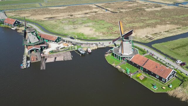 Aerial view of a traditional windmill and buildings with red rooftops casting shadows alongside the dark water, Zaandam, Noord-Holland, Netherlands.