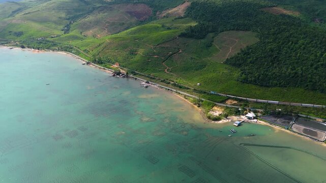Aerial view of the coastline with a train running alongside the lush green hills meeting the turquoise waters of Trinh To Tam, tt. Lang Co, Hue, Vietnam.
