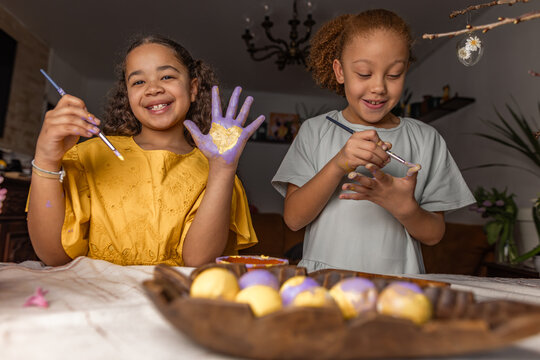 Siblings painting Easter eggs together in a cheerful home setting