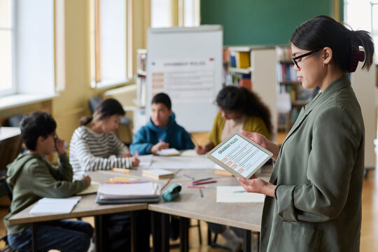 Young teacher using digital tablet while conducting group language class