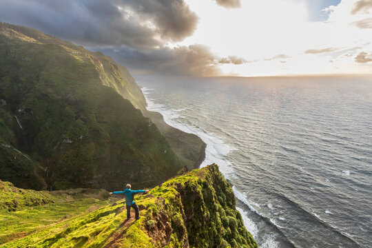 Tourist at cliff edge overlooking Madeira coastline at sunset