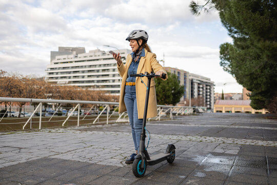 Senior woman using smartphone while standing with electric scooter outdoors
