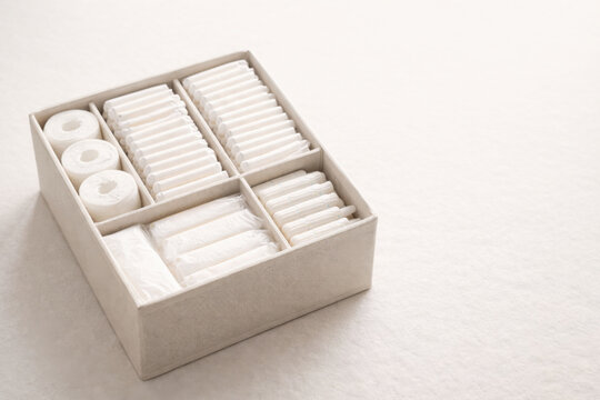 Neutral toned organizer box with neatly arranged tampons, pads, and cotton rolls, showcasing minimalist storage and clean personal care organization.