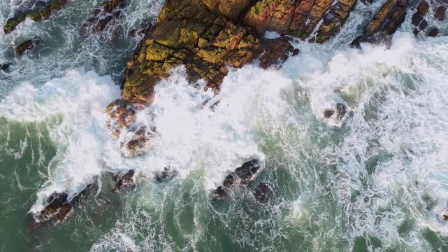 Aerial view of waves crashing against the rocky shore, contrasting the rough textures of the rocks with the smooth, foamy sea, Bai Xep, Binh Dinh, Vietnam.