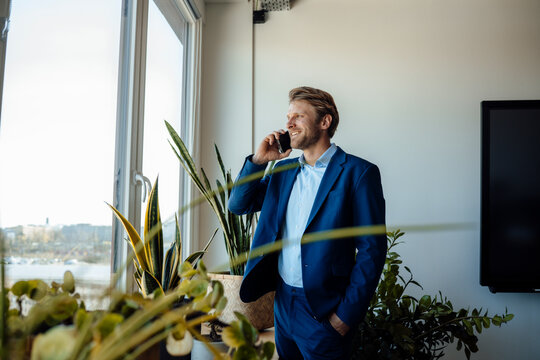 Businessman in suit talking on phone by office window with plants