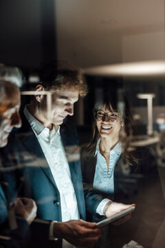 Team collaborating in modern office at night with tablet and glass reflection