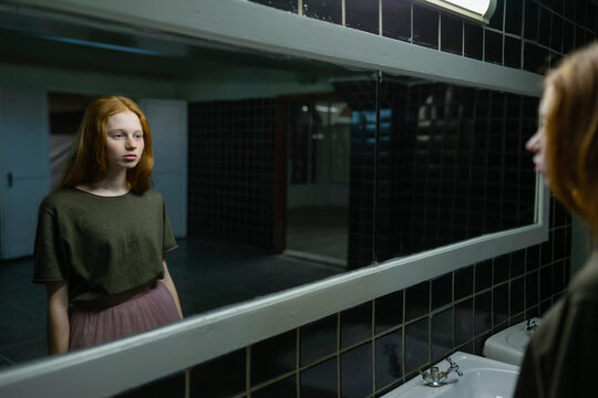 Red haired woman with freckles looking at reflection in bathroom mirror