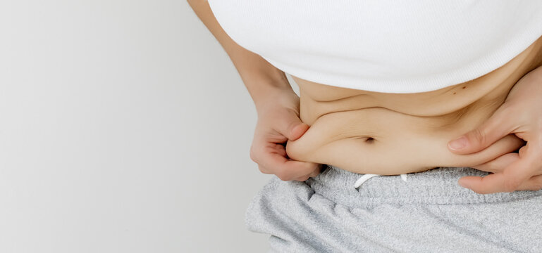 Close-Up of Woman's Hands Pinching Belly Fat Skin Fold at Waist in White Crop Top and Gray skirt &mdash; Female Checking Abdominal Subcutaneous Fat, Body Weight Awareness, Healthy Lifestyle Motivation