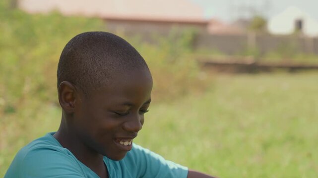 Black boy smiling after playful match sunlit grassy field turquoise shirt relaxed posture reflective joy candid closeup aspiring striker vibe community game memory warm natural light