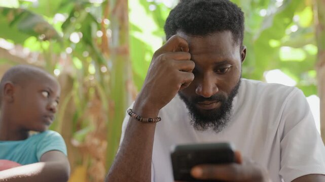 Black father checking phone with son. Outdoor garden scene with white shirt bearded father reading smartphone, notification inducing surprise and worry, child looking on, digital distraction creating