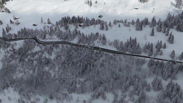 Aerial view of a road winding through a snow-covered forest, with scattered cabins dotting the landscape, Ormont-Dessus, Vaud, Switzerland.