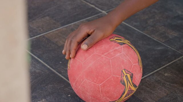 Hand placing red soccer ball on tile, black youth palm sets ball on tiled court, pregame focus and calm, authentic urban preparation for street match with textured scuffed surface