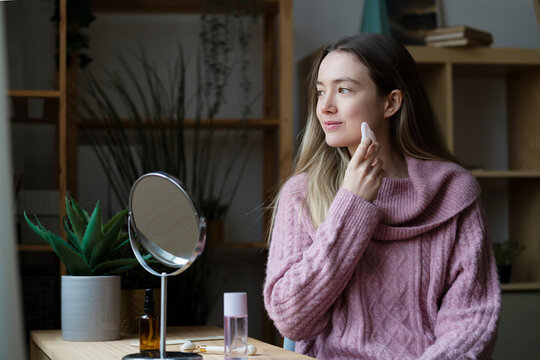 Woman applying skincare routine at home with mirror and cosmetics