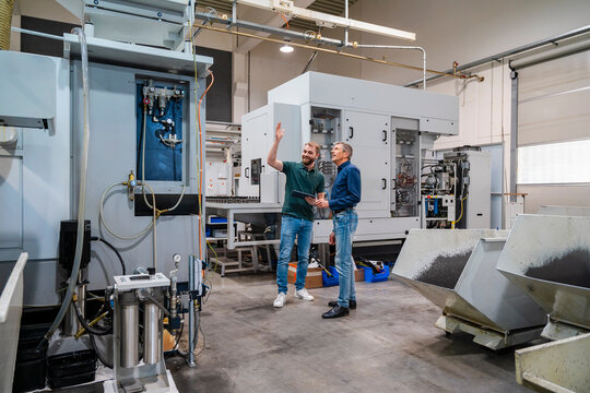 Two men discussing in a production hall with industrial machinery