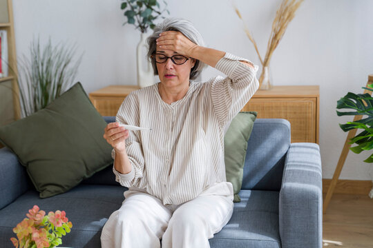 Woman checking temperature with thermometer at home on sofa
