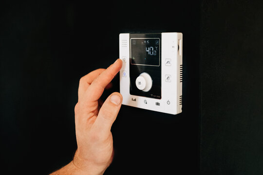 Hand adjusting smart thermostat on wall in modern home