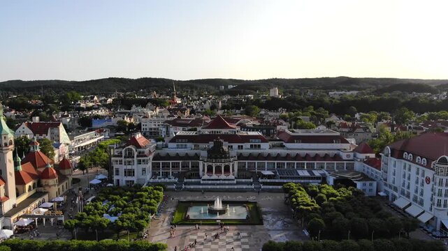 Aerial view of the iconic Grand Hotel and Sopot pier, with crowds enjoying the manicured gardens and beachfront in the distance, Sopot, Pomeranian Voivodeship, Poland.