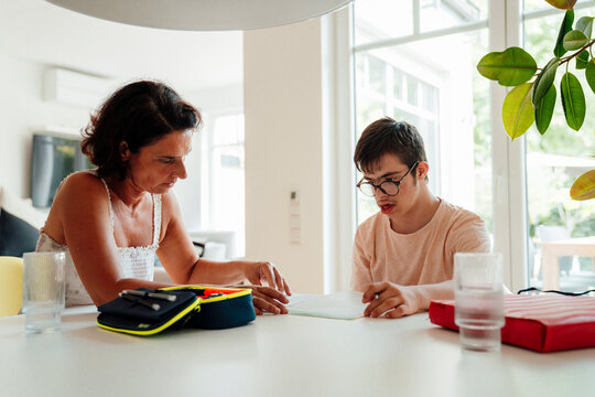 Mother supporting son with trisomy 21 doing homework at home