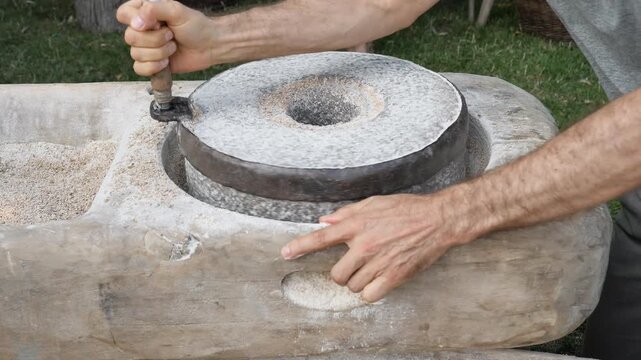 Historical Milling Process. Man Grinding Rye Flour with Hand Operated Stone Quern.